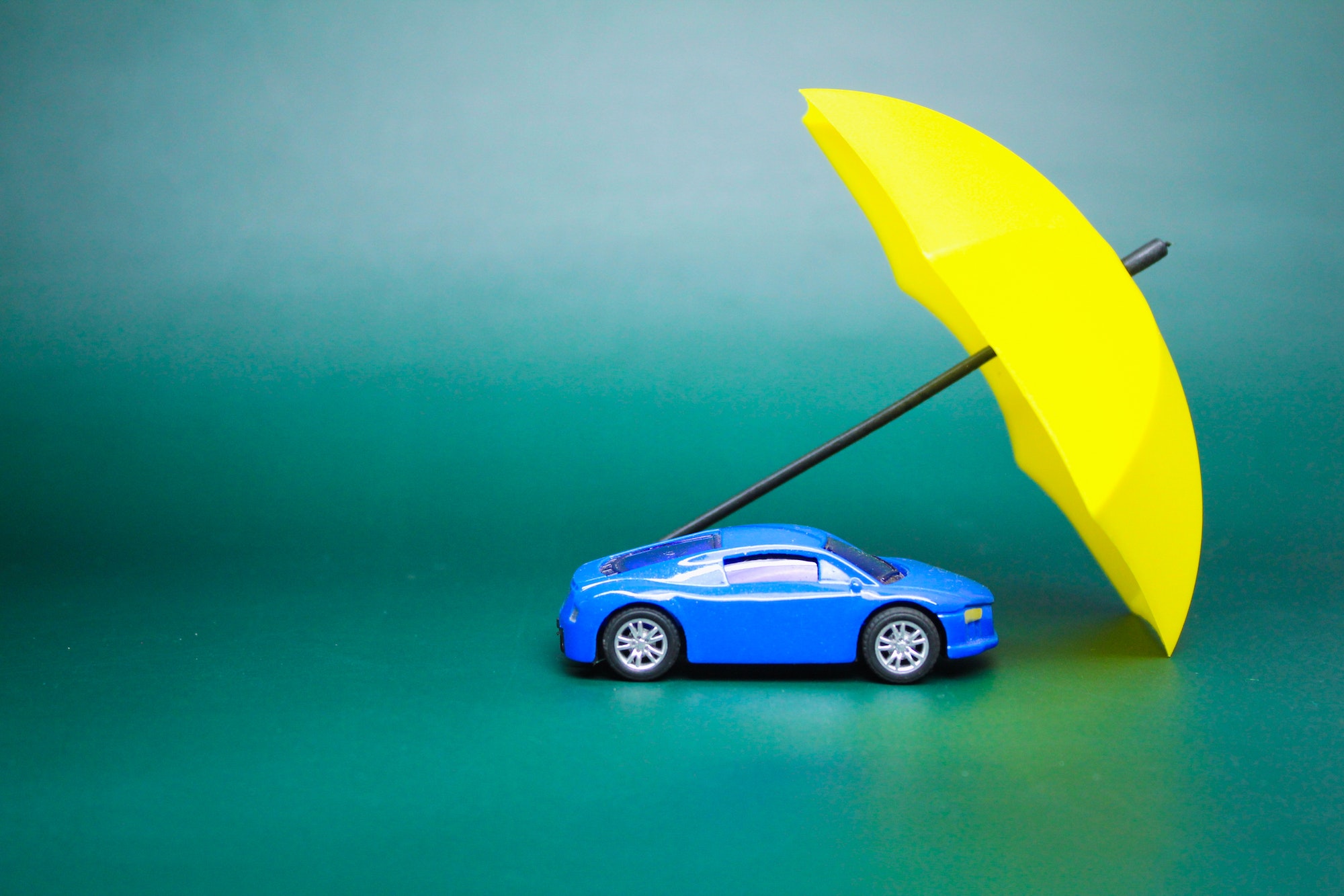 small car model covered by an umbrella. vehicle insurance concept